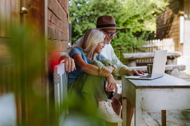 Elderly woman sitting beside her senior husband who is working on laptop.